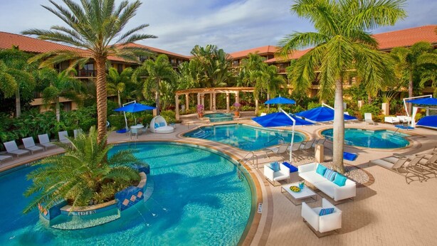A resort pool area with multiple pools, lounge chairs, and palm trees.