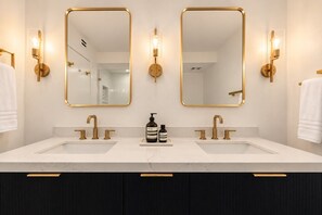 A modern bathroom with two sinks, gold fixtures, and wall-mounted mirrors.