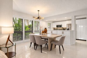 Una cocina moderna con armarios blancos, una isla central y un comedor con sillas.