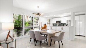 A modern kitchen with white cabinets, a central island, and a dining area with a glass table and chairs.