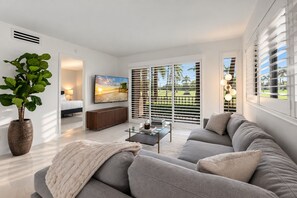 A modern living room with a sofa, a coffee table, a TV, and a large window with blinds.