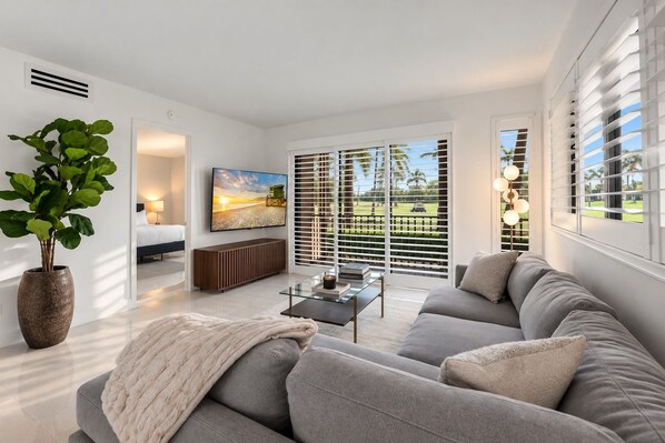 A modern living room with a sofa, a coffee table, a TV, and a large window with blinds.