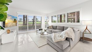 A modern living room with a grey sofa, a glass coffee table, and a white rug.