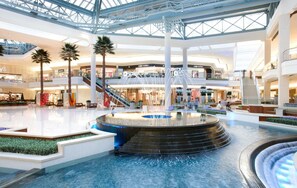 A spacious indoor atrium with a central water feature, multiple levels, and retail stores.