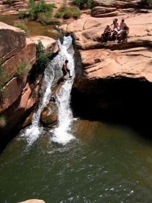 A waterfall in a rocky canyon with a group of people sitting on the rocks. - Southwest Charm and Amazing Views, just minutes from town! (Moab)