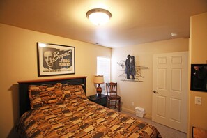 A bedroom with a patterned bedspread, a framed picture on the wall, a chair, a nightstand, a lamp, and a door. - Southwest Charm and Amazing Views, just minutes from town! (Moab)