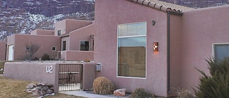 A modern building with a pink facade, a gated entrance, and a view of a mountainous landscape.