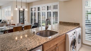 A kitchen with granite countertops, a stainless steel sink, a built-in washing machine, and a dining area with a table set for four.