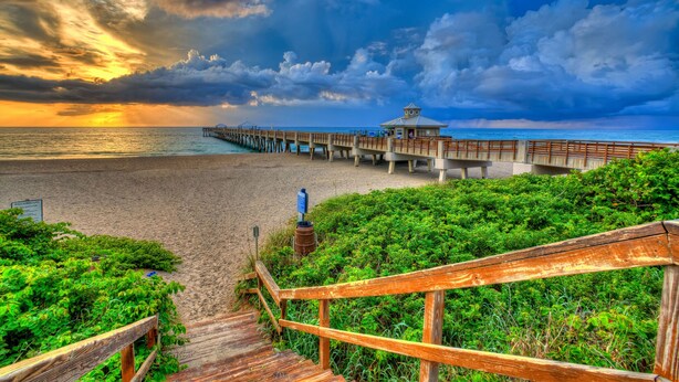 A wooden pier extending into a beach with a gazebo at the end.