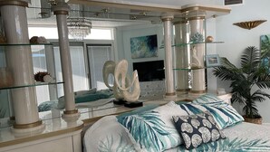 Ein Schlafzimmer mit einem großen Bett, einem Glastisch, einem Fernseher und einem großen Fenster mit Jalousien.