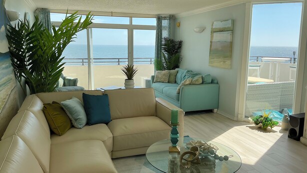 Ein Wohnzimmer mit einem beigefarbenen Sofa, einem Glastisch und Blick auf den Ozean.