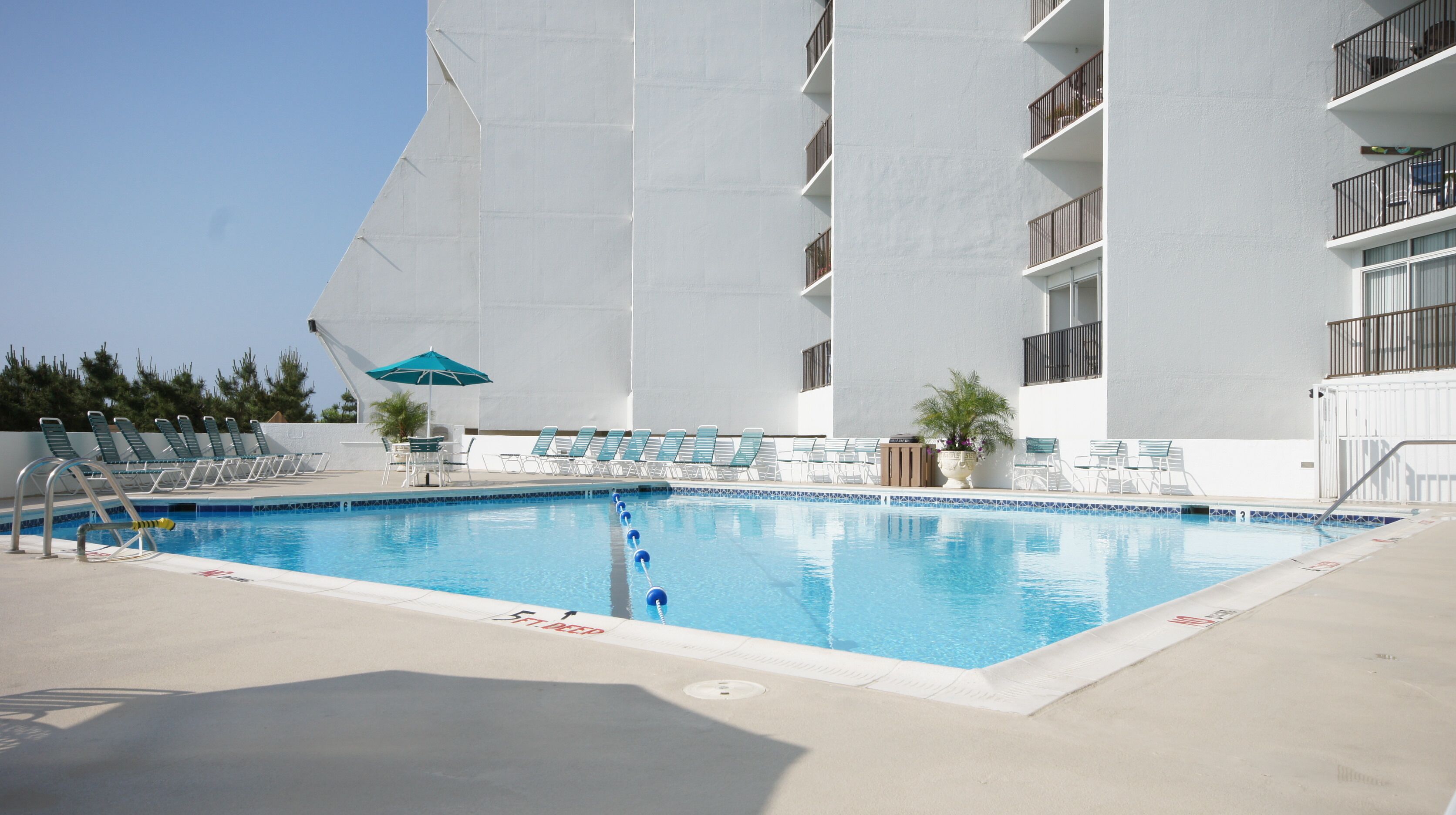 Una piscina con lettini e ombrelloni, circondata da un edificio bianco con balconi.
