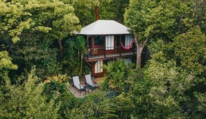 Een huis met twee verdiepingen, omringd door weelderige begroeiing, met een balkon en een terras.