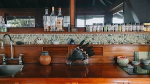 Una cocina con protector contra salpicaduras de piedra, armarios de madera, un lavamanos y diversos utensilios de cocina y botellas.