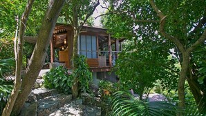 Una casa tradicional japonesa con estructura de madera, rodeada de abundante vegetación y senderos de piedra.