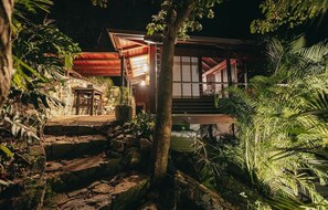 Een traditioneel Japans gebouw met een pad van stenen dat naar de ingang leidt, omgeven door weelderige begroeiing.
