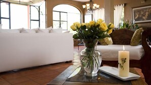 Ein Zimmer mit einem weißen Sofa, einer Glasvase mit gelben Blumen und einer Kerze auf einem Tisch.