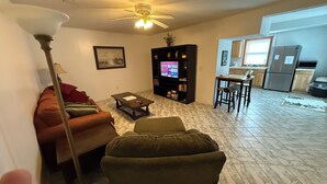 A living room with a sofa, armchair, coffee table, and a TV. There's a bookshelf, a dining area with a table and chairs, and a kitchen with a refrigerator and stove. - Apartment in town (Franklin)