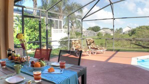 Un patio cubierto con una mesa preparada para el desayuno, sillas y vistas a una piscina y vegetación.