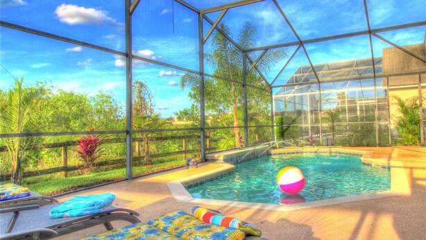 Una piscina interior con paredes de vidrio transparente, rodeada de exuberante vegetación y un cielo soleado.