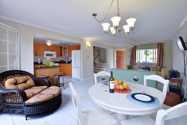A dining area with a round table set for four, a wicker sofa, and a kitchen in the background.