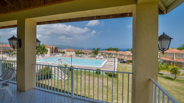 Un balcon donnant sur une piscine, avec des balustrades blanches et un ciel dégagé.