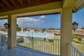 A balcony with a view of a swimming pool, white railings, and a clear sky.