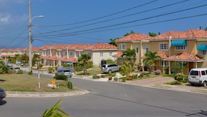 Une rue résidentielle bordée de maisons aux toits recouverts de tuiles rouges, avec un ciel d’un bleu éclatant.