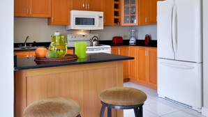 Une cuisine avec des meubles en bois, un réfrigérateur blanc, un four à micro-ondes et deux tabourets.