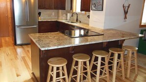 A kitchen with wooden cabinets, a stainless steel refrigerator, a granite countertop, and wooden stools.