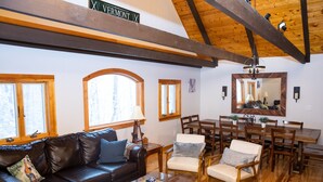 A living room with a brown leather sofa, two armchairs, a wooden dining table with chairs, and large windows.