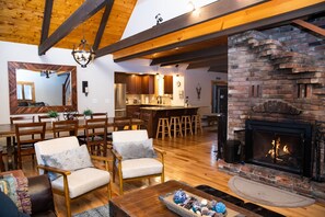 A spacious living room with wooden floors, a fireplace, and a dining area with wooden furniture. - Private Home on Okemo with HOT TUB. WALK TO SKI TRAIL OR DRIVE 2 MIN TO LODGE (Ludlow)