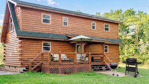 Une cabane en rondins avec une terrasse, un espace salon extérieur et un barbecue.