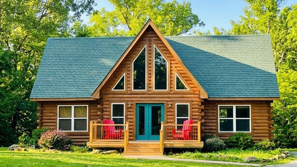 Une cabane en rondins avec un porche à l’avant, deux fenêtres sur le côté et une porte verte.