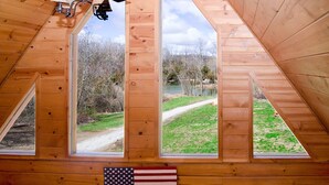 Une chambre mansardée triangulaire avec trois fenêtres donnant sur un espace verdoyant et des arbres.