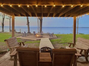 An outdoor seating area with wooden benches and chairs, a fire pit, and a view of the water.