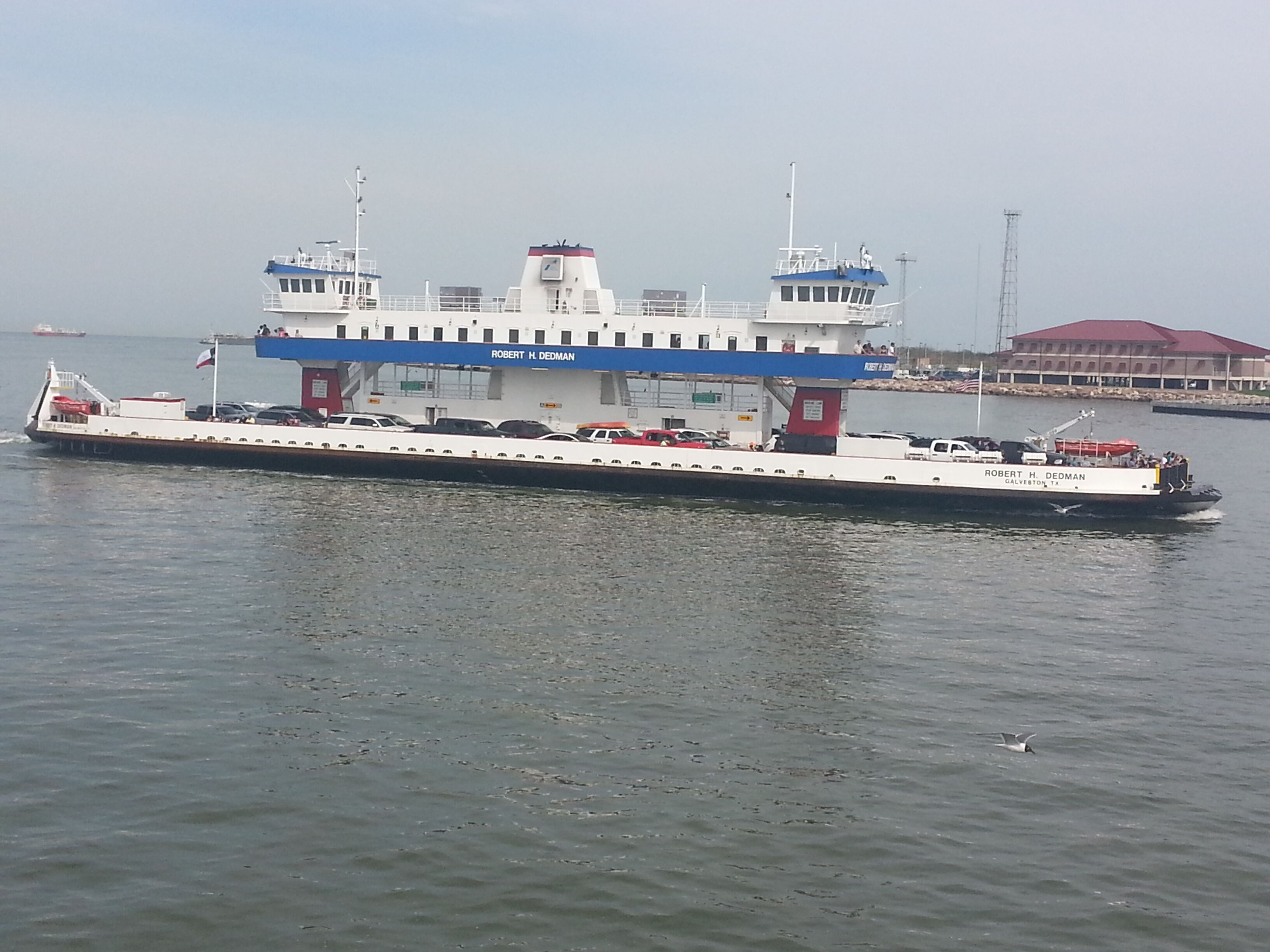 A ferry with multiple decks and a flat roof, traveling on water.