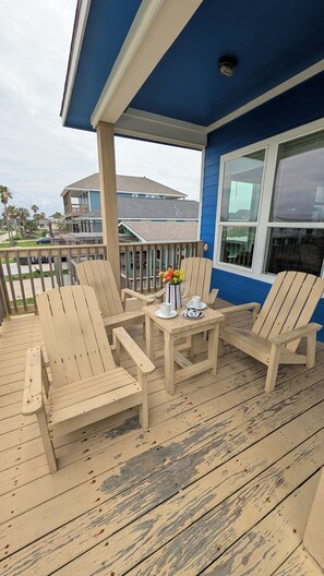 A wooden deck with chairs and a table, a blue house, and a view of other houses.