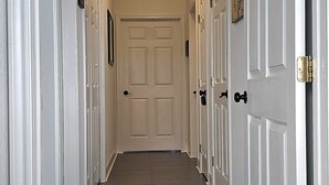 Un couloir avec des portes blanches, un luminaire au plafond et un plancher en bois.