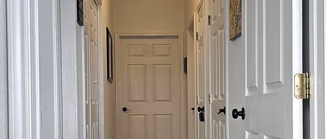 A hallway with white doors, a ceiling light, and a wooden floor.