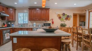 A kitchen with wooden cabinets, a central island with stools, a microwave, and a decorative wall plate. - Cozy Vacation home-3 bedrooms/2 bath- 1 mile to Disney Parking Tram (Anaheim)