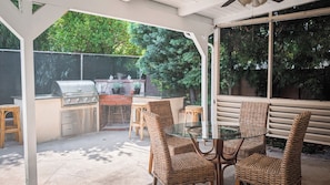 An outdoor patio with a grill, wicker chairs, and a glass table.