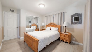 A bedroom with a wooden bed, two bedside tables with lamps, a mirror, and a door.