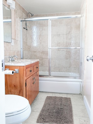 A bathroom with a shower, toilet, vanity, and a rug.