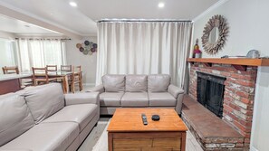 A living room with a sofa, a coffee table, a fireplace, and a dining area with chairs and a table.