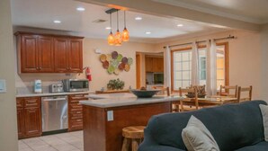 A modern kitchen with wooden cabinets, a central island, and a dining area with a table and chairs. - Cozy Vacation home-3 bedrooms/2 bath- 1 mile to Disney Parking Tram (Anaheim)