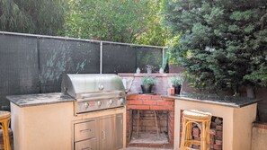 An outdoor kitchen with a grill, a sink, and a stool.