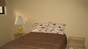 Une chambre à coucher avec une couvre-lit marron, une lampe jaune sur une table de chevet et une table de nuit en osier.