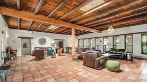 A spacious living area with a high wooden ceiling, tiled floor, and large windows.