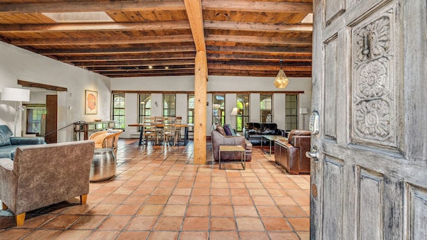 A spacious living area with wooden beams, a dining set, and a large door with intricate carvings.